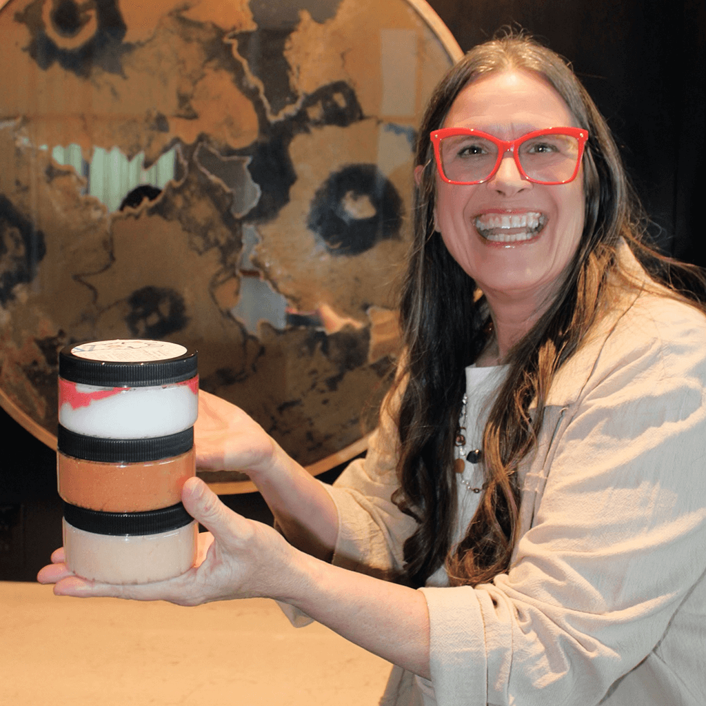 Photo of one of the partners, Paulette, holding a stack of sugar body scrub jars and laughing. AlpacaSoaps Alpaca Soaps